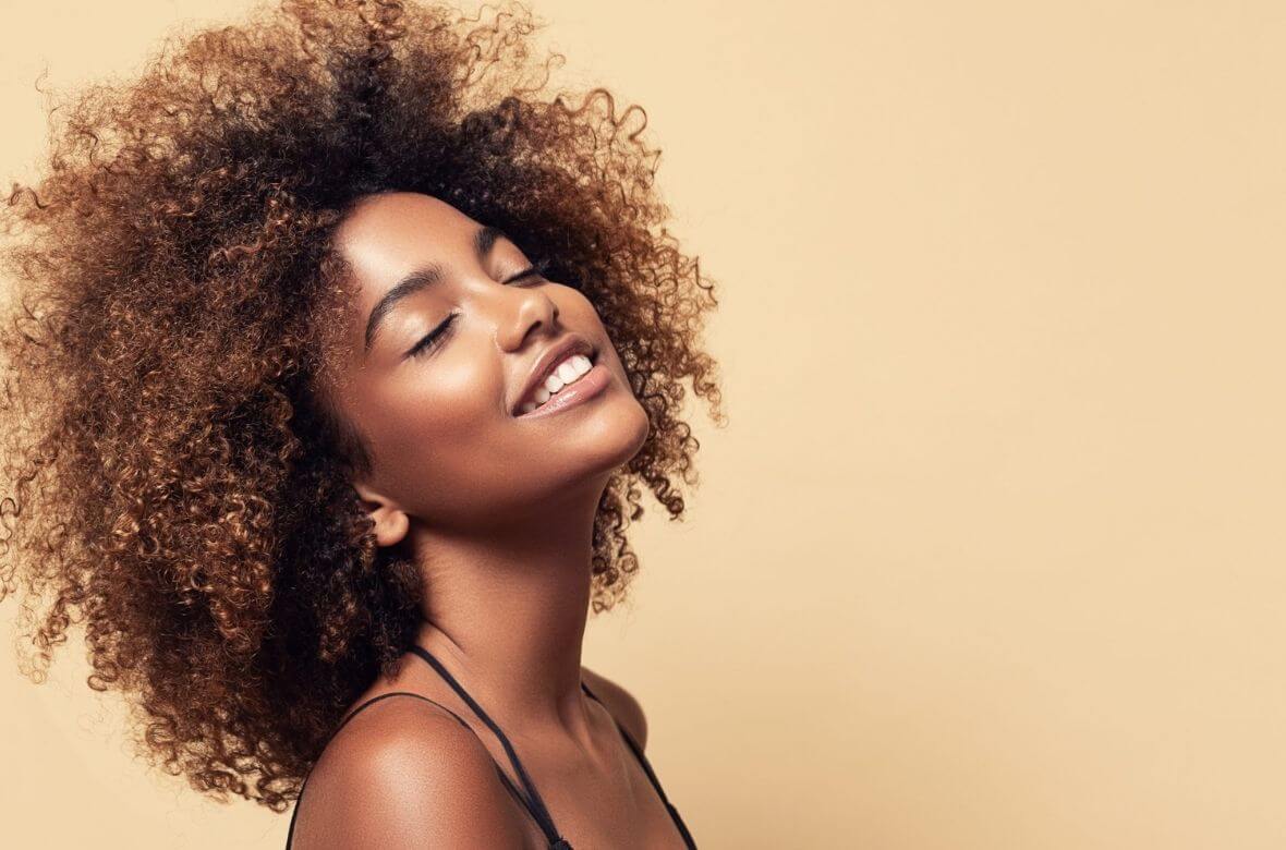 Mulher sorri confortavelmente ao exibir seus cabelos saudáveis e volumosos