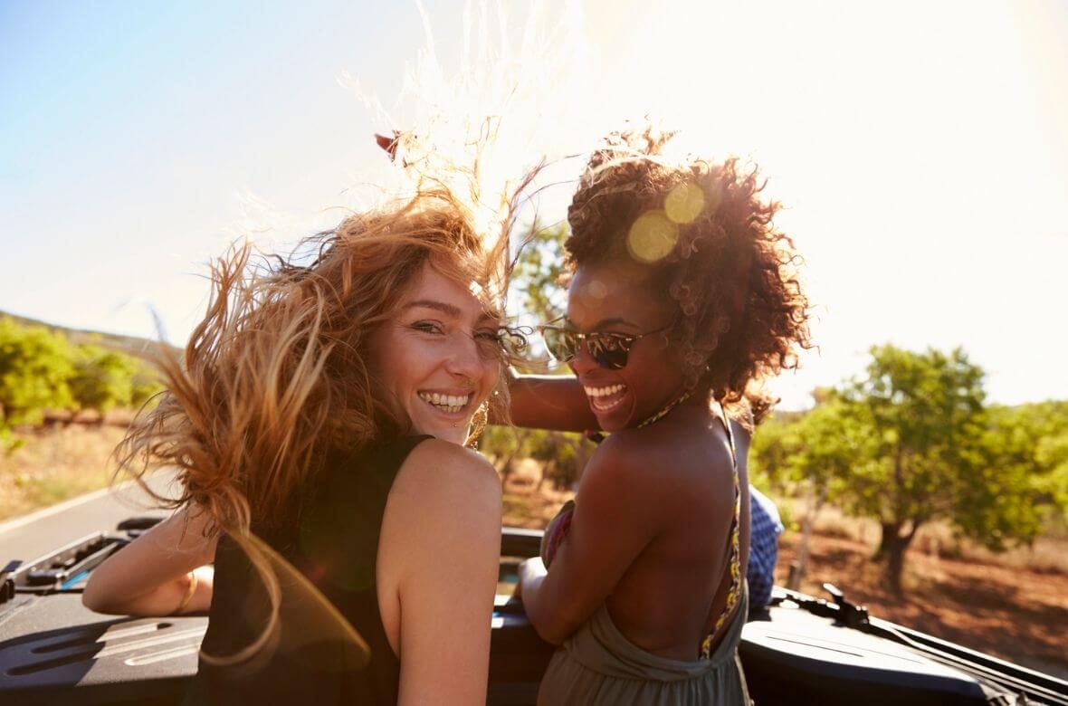 Duas mulheres sorriem em uma viagem de carro em um dia ensolarado
