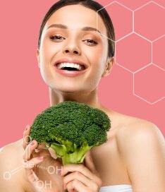 Mulher sorrindo e segurando uma cabeça de brócolis em suas mãos. A imagem representa a presença de zinco, cromo e selênio no brócolis, assim como nas cápsulas de Spax.